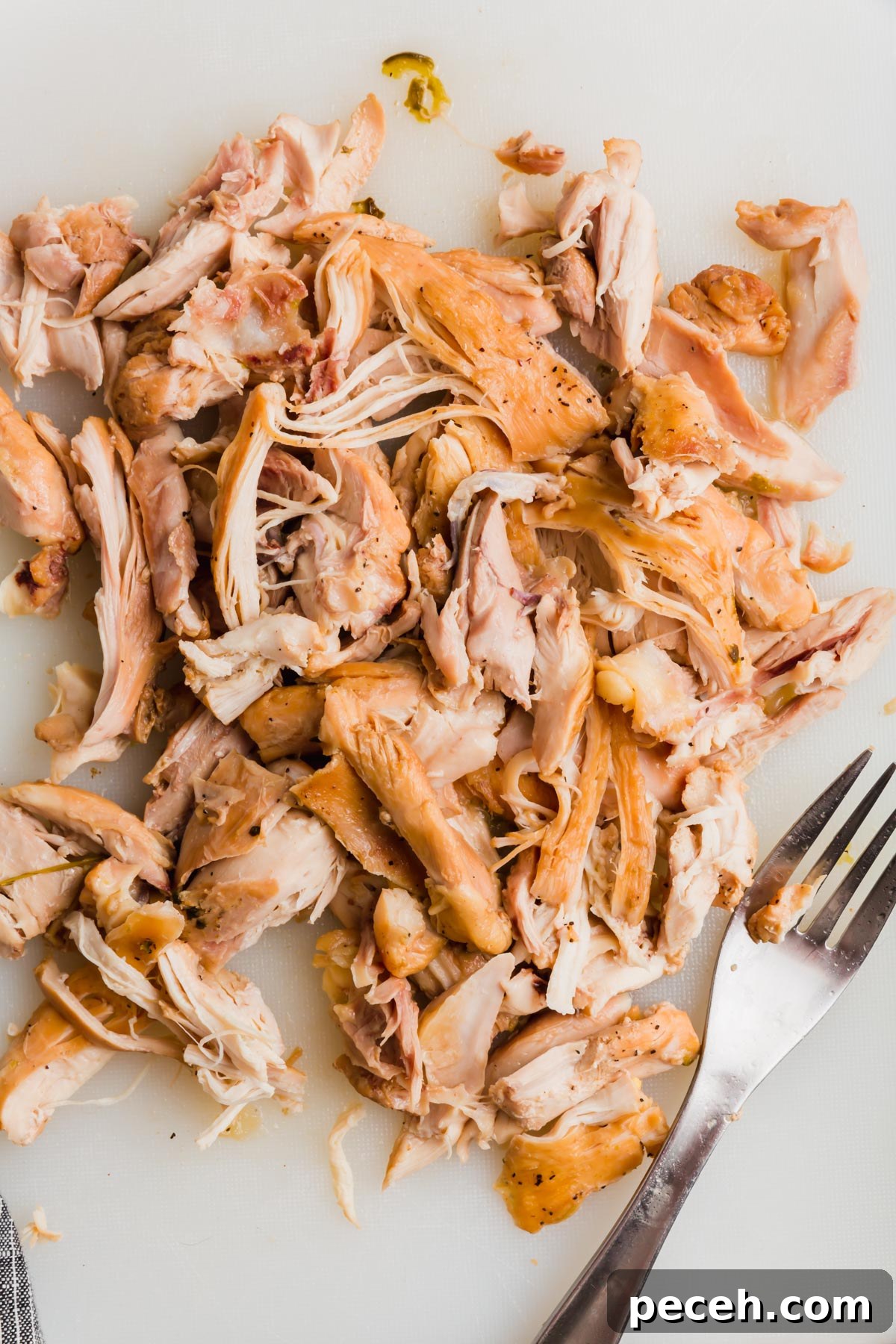 Roasted Chicken and Poblano Soup Recipe 11 Shredded chicken thighs on a white cutting board with a fork.