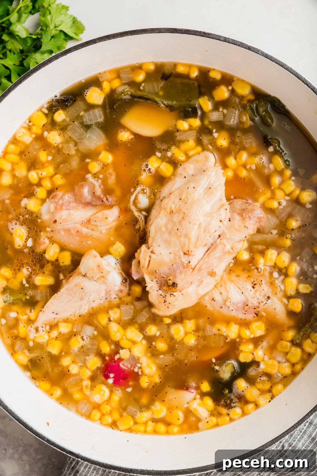 Roasted Chicken and Poblano Soup Recipe 10 An overhead view of a white dutch oven with poblano corn soup topped with cooked chicken thighs.