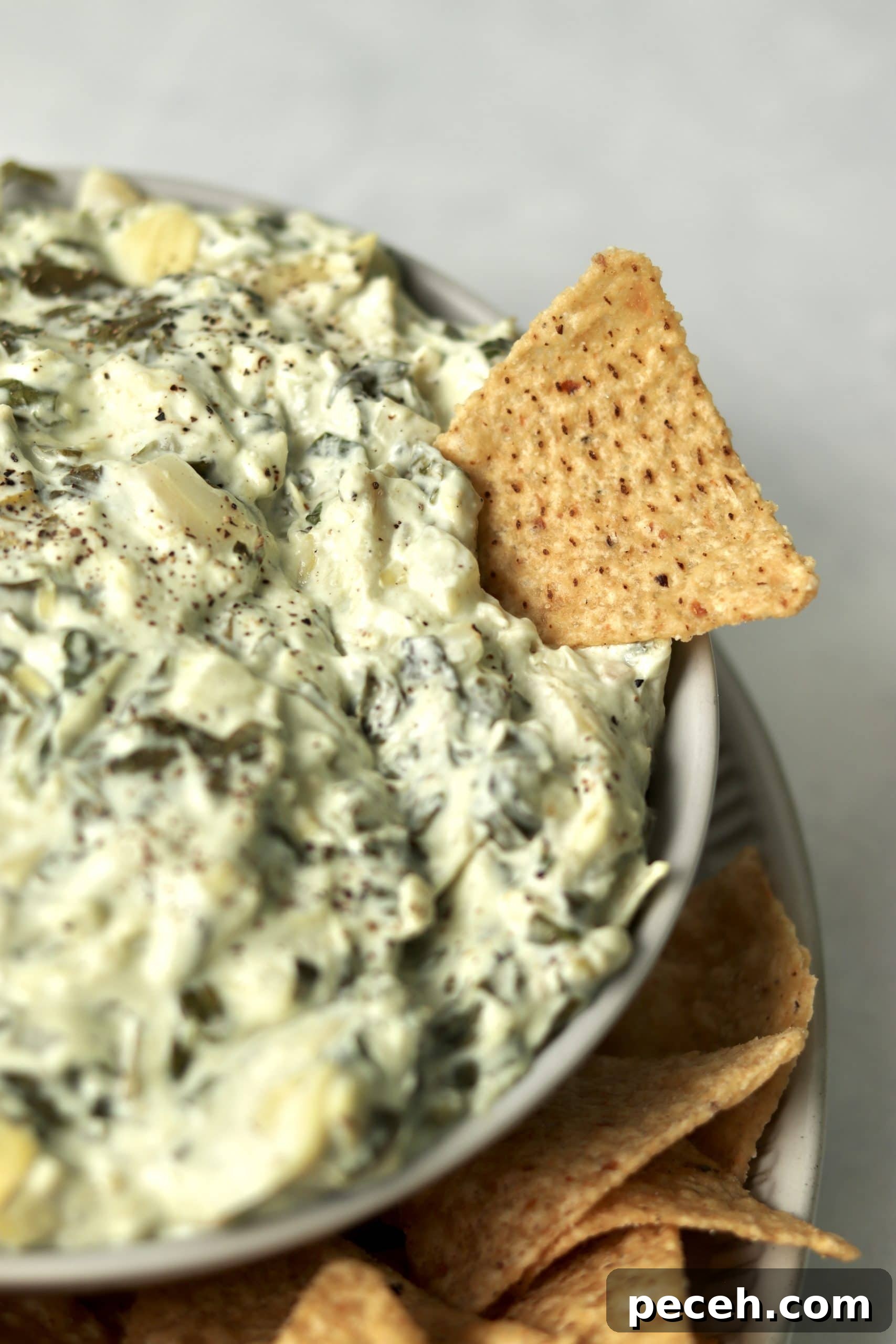 Tortilla chip being dipped into spinach artichoke dip