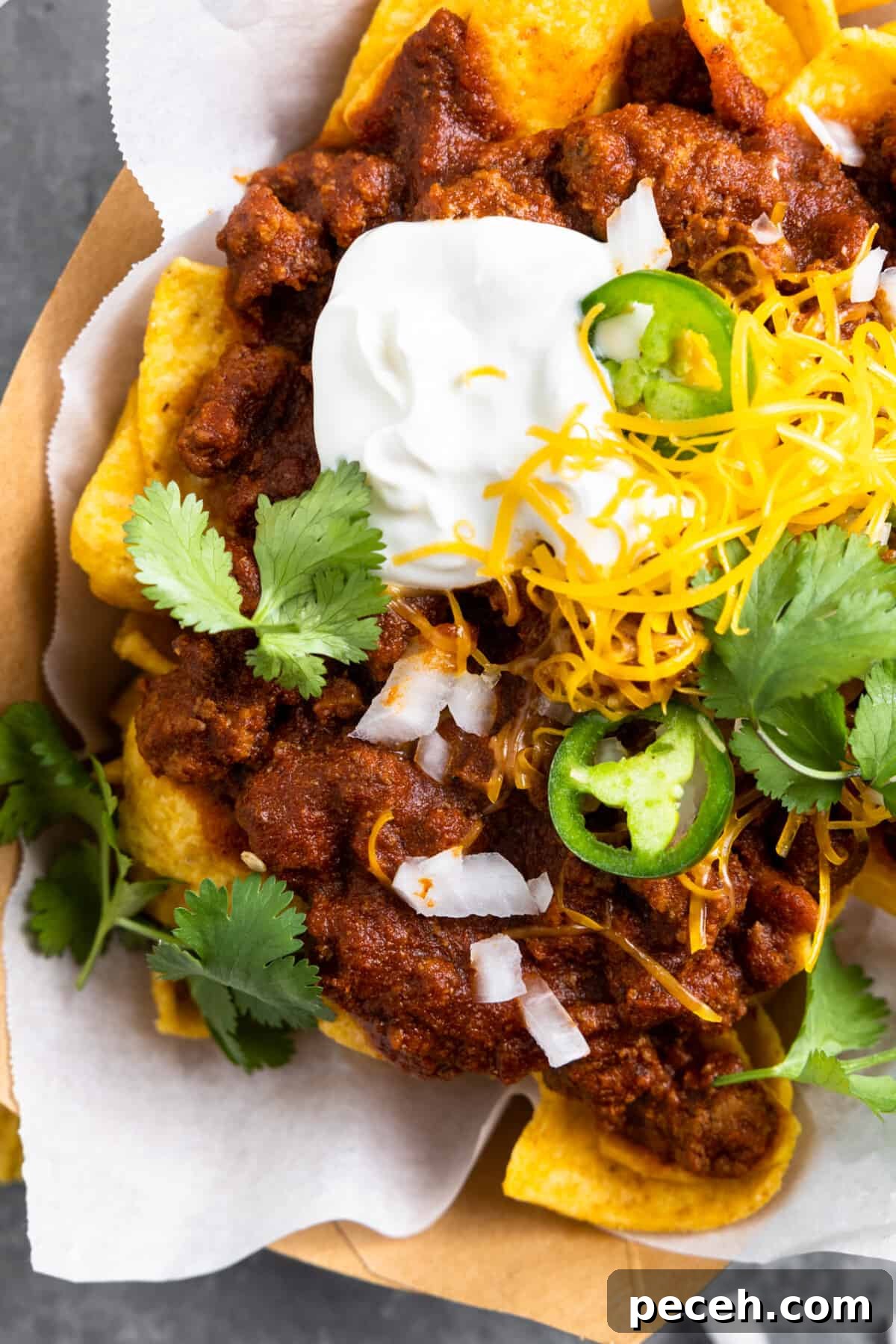 Ground beef chili on top of Fritos for a Texas style Frito pie served in a cardboard boat with sour cream.