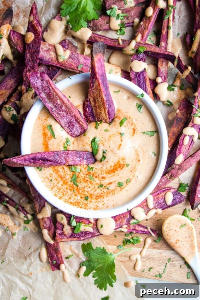 Smoky Chipotle Salad Dressing Recipe: Zesty, Creamy, & Homemade 8 Purple sweet potato fries surrounding a small white bowl of chipotle mayo sauce that's also drizzled onto the fries. A few fries are dipping into the sauce that's sprinkled with additional chipotle powder and chopped fresh cilantro.