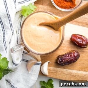 Smoky Chipotle Salad Dressing Recipe: Zesty, Creamy, & Homemade 10 Small glass pitcher filled with orange creamy salad dressing, there are a couple of dates, a few cloves of garlic, some sprigs of cilantro and a small dish of chipotle powder surrounding the dressing that's on top of a wooden cutting board.