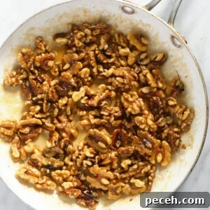 Candied Walnuts Recipe: Crunchy Sweet Coated Nuts in 20 Minutes 8 walnuts in a frying pan on a marble countertop.