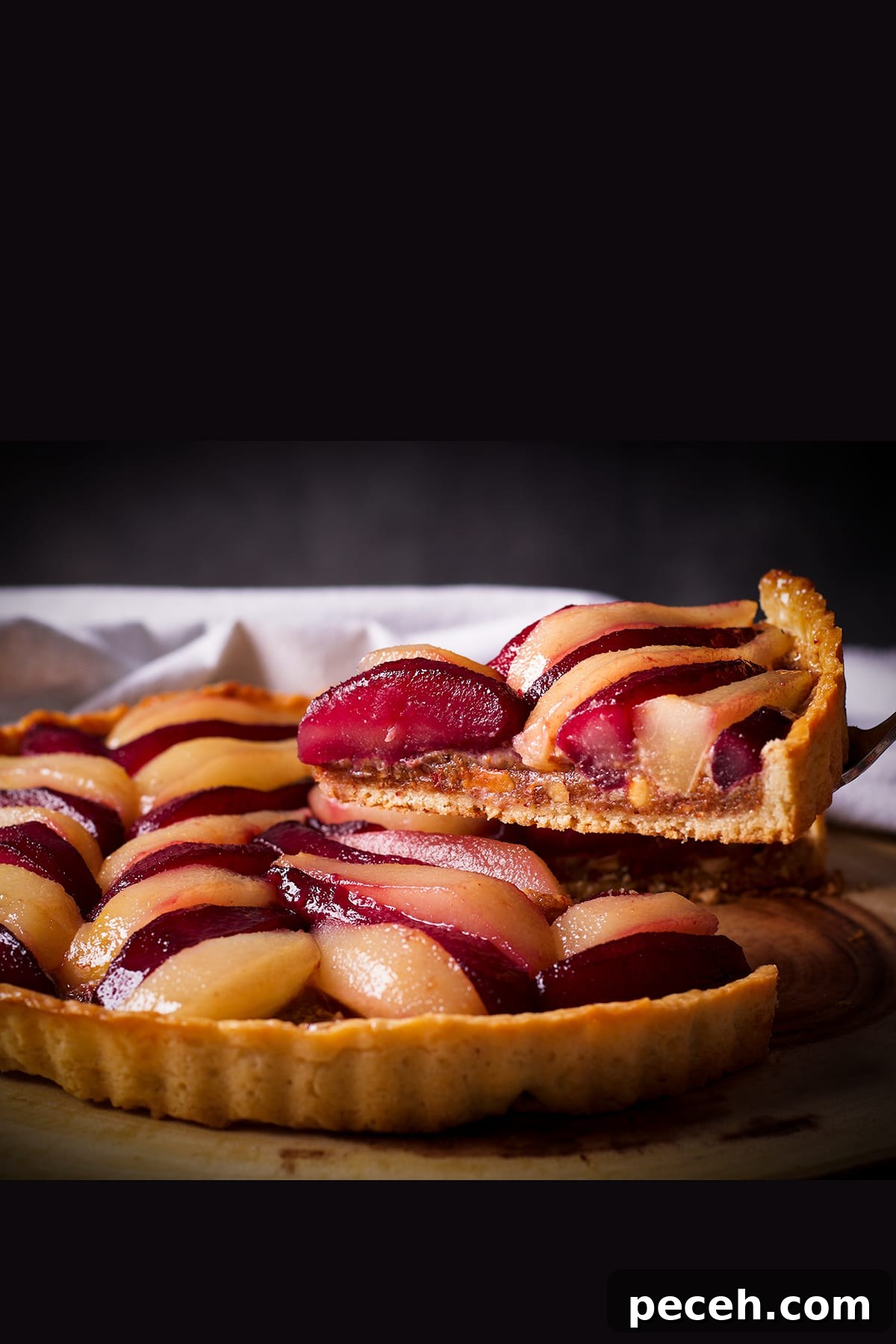 Someone using a pie server to lift a slice of poached pear and frangipane tart from a serving platter.