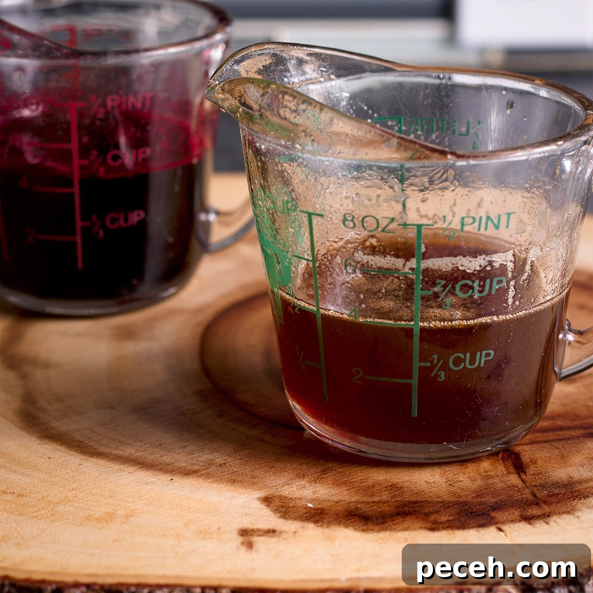 Two measuring cups containing poached pear wine reduction.