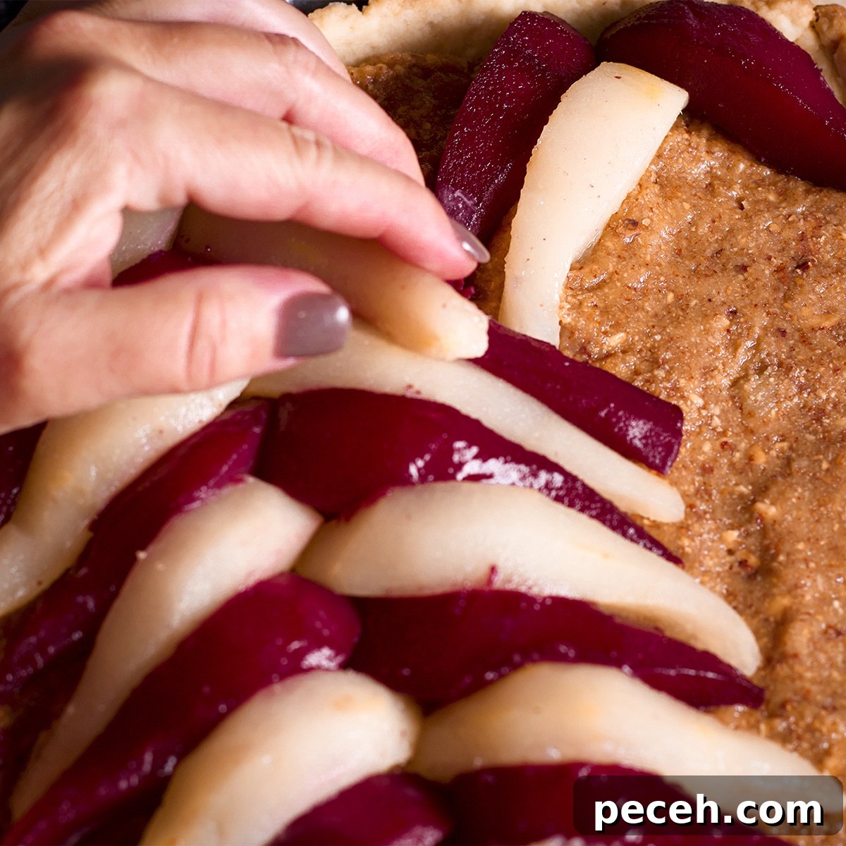 Someone using their hand to arrange wine poached pears over a tart filled with frangipane. 