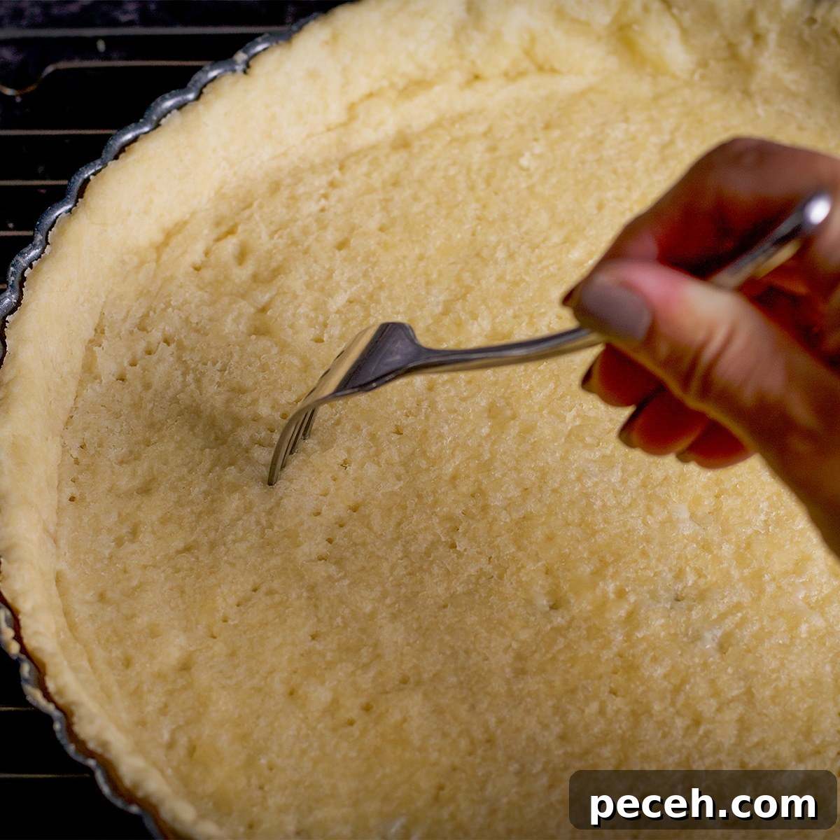 Someone using a fork to poke holes in tart crust dough.