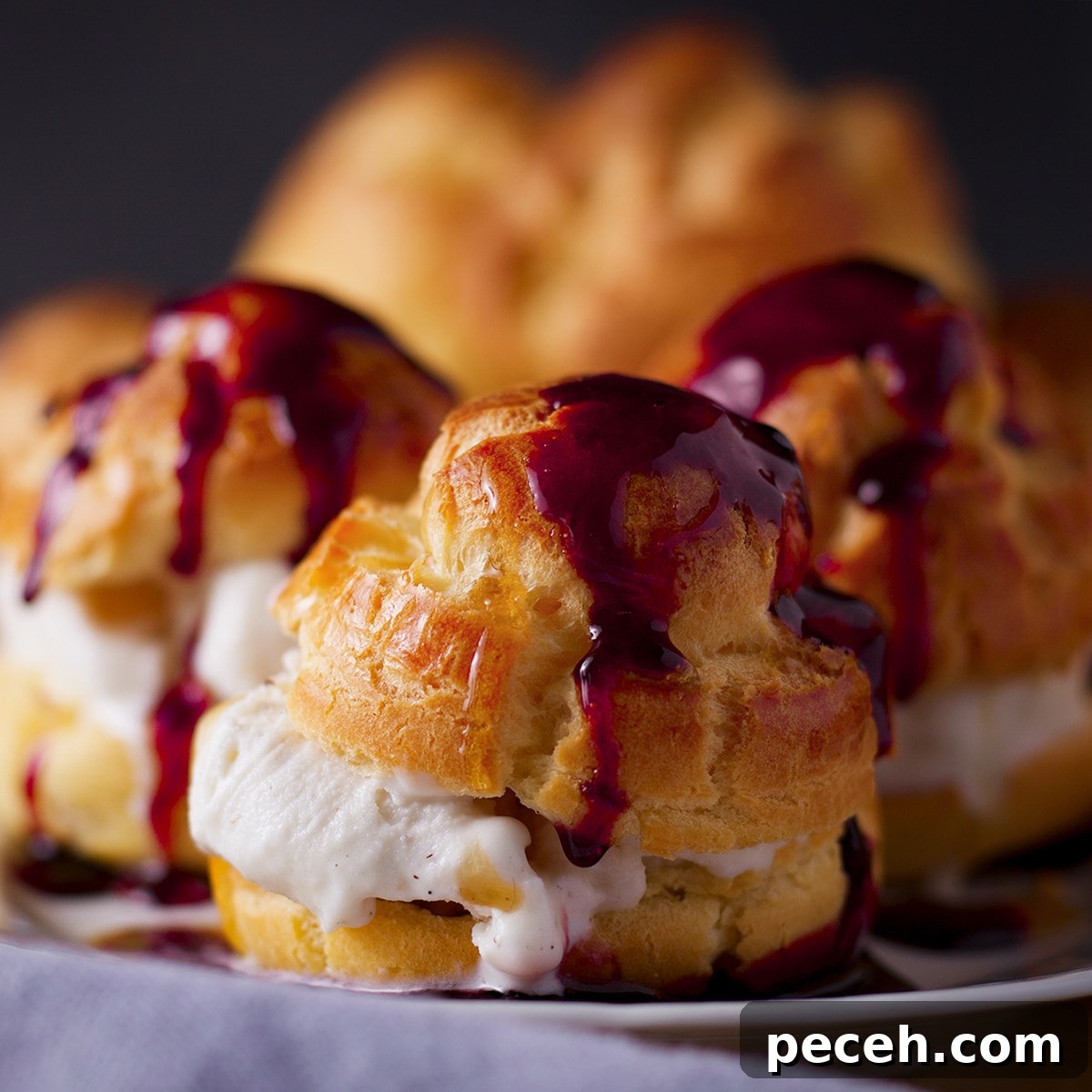 A tray of ice cream filled profiteroles that have been drizzled with red wine dessert sauce.