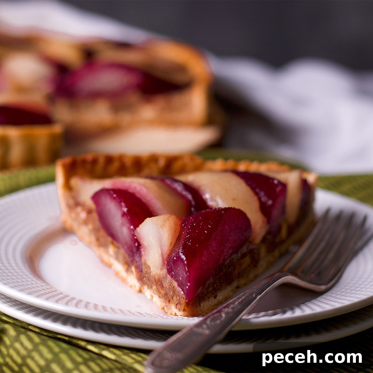 A slice of poached pear and frangipane tart on a white plate with a fork.