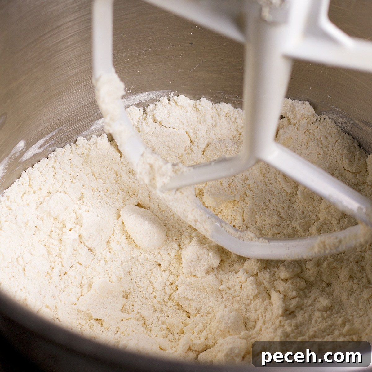 Looking down into the bowl of a stand mixer containing flour that's been mixed with cold butter.