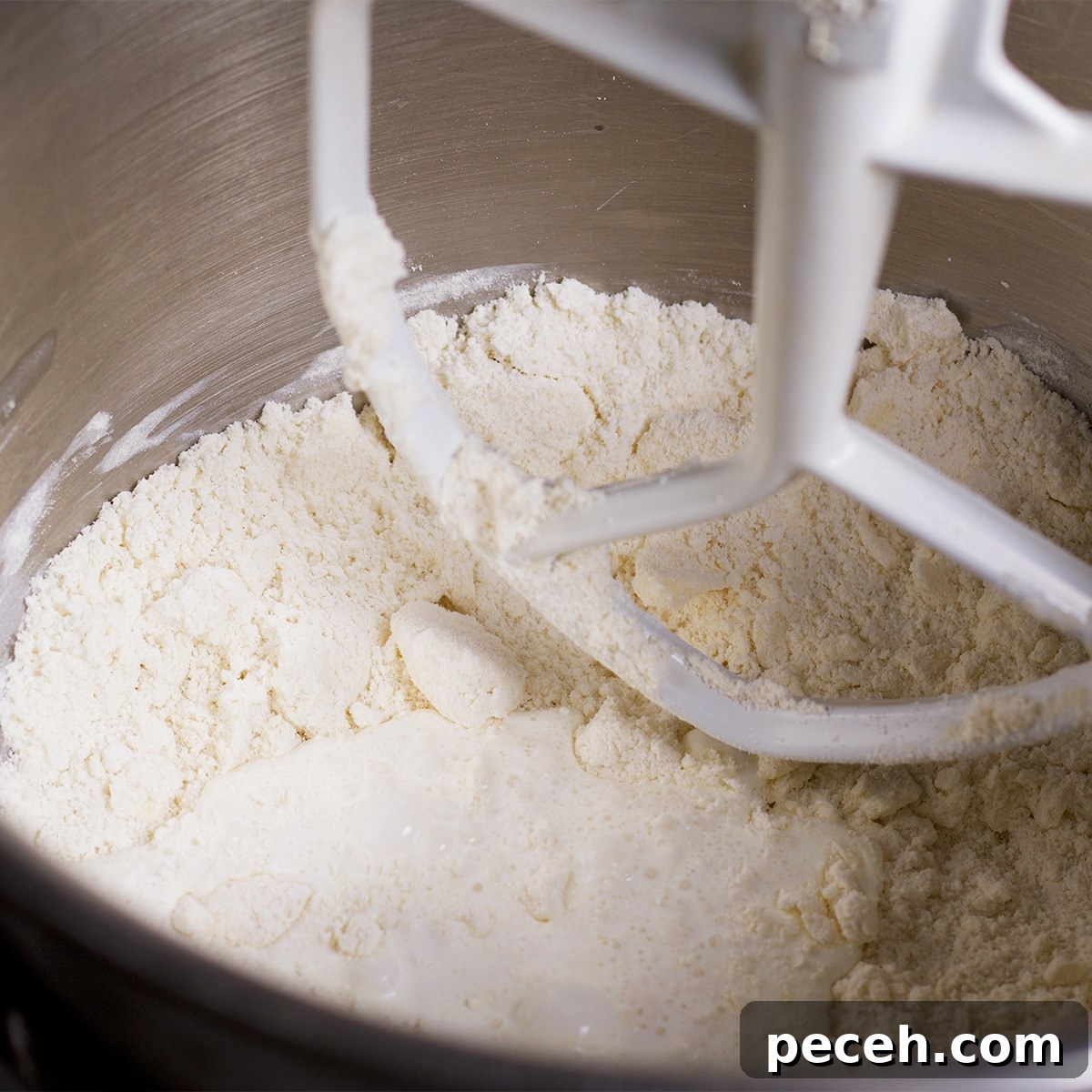 Adding cream to the flour and butter mixture as it mixes together in the bowl of a stand mixer.