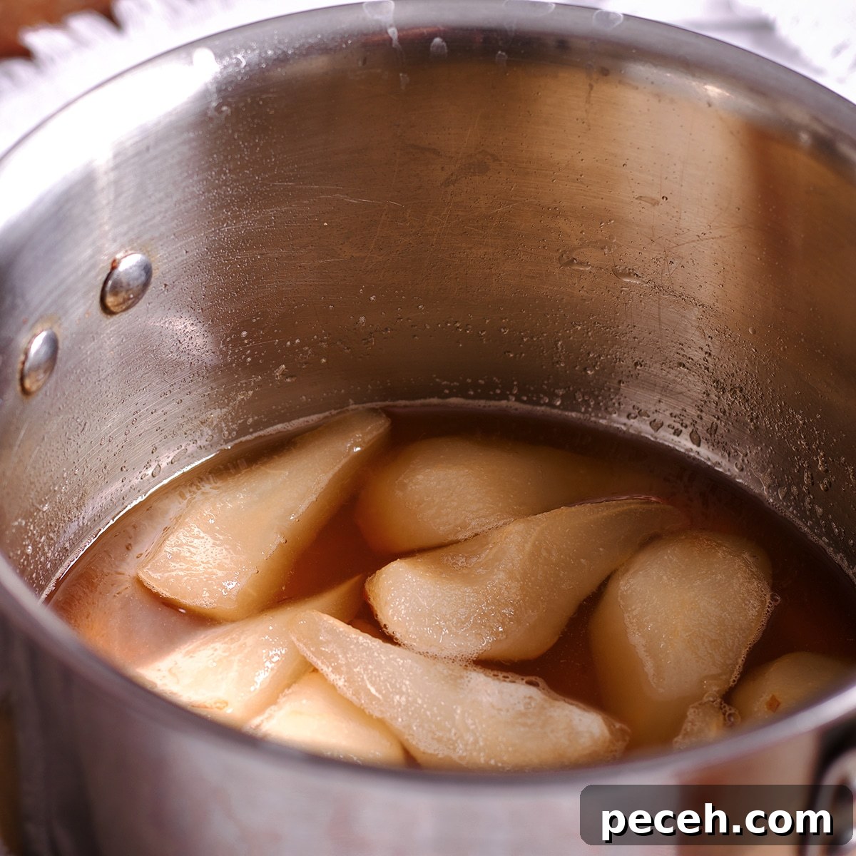 A saucepan containing white wine and sliced pears.