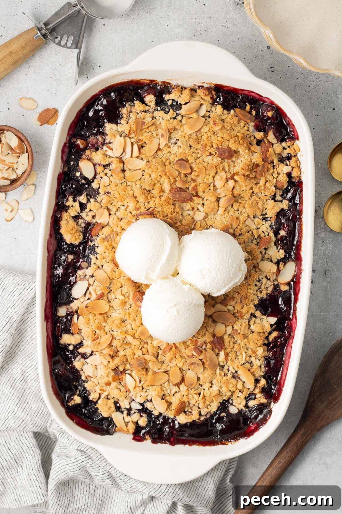 Three scoops of ice cream on top of cherry crisp in a white baking pan.