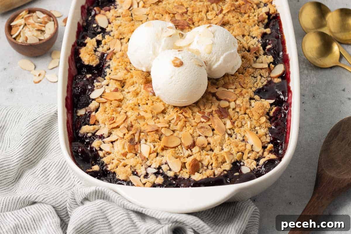 Three scoops of ice cream on top of cherry crisp in a white baking dish.
