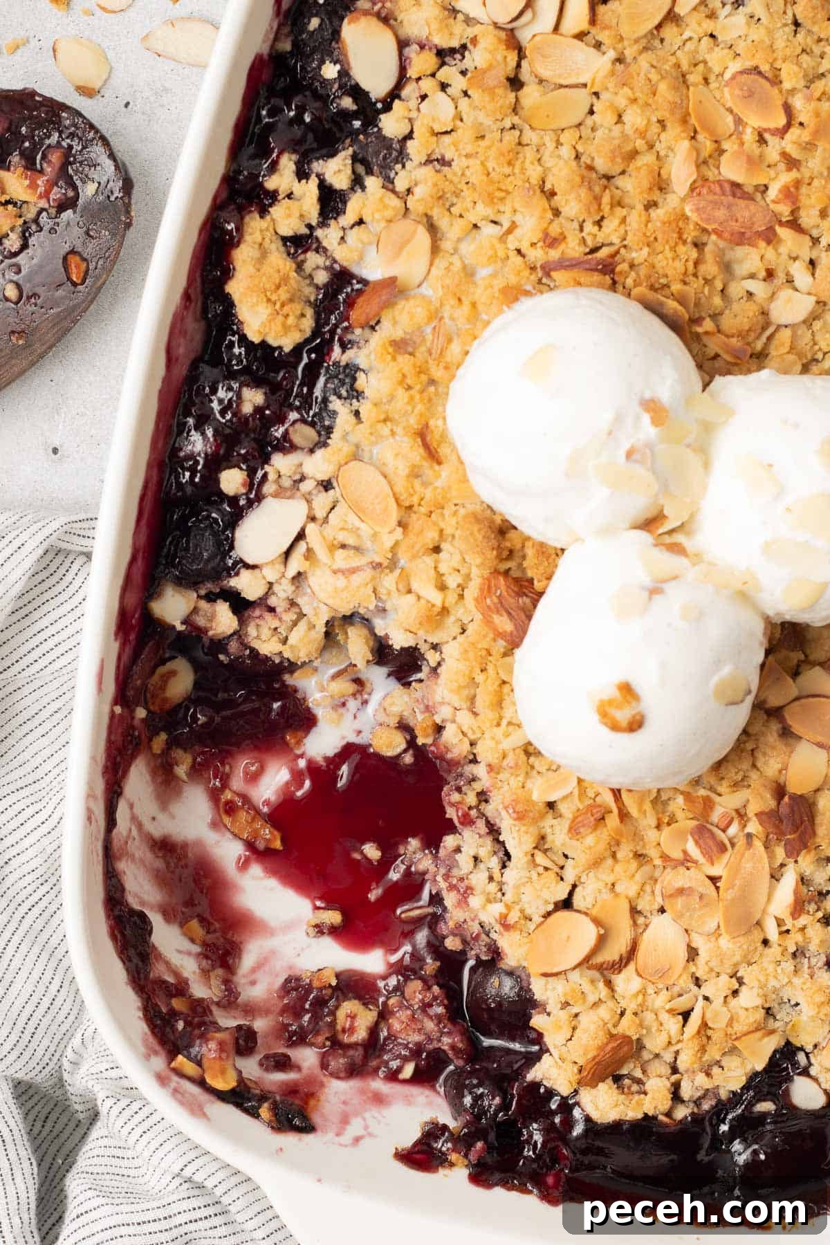 A baking dish of cherry crisp with ice cream with a scoop missing.