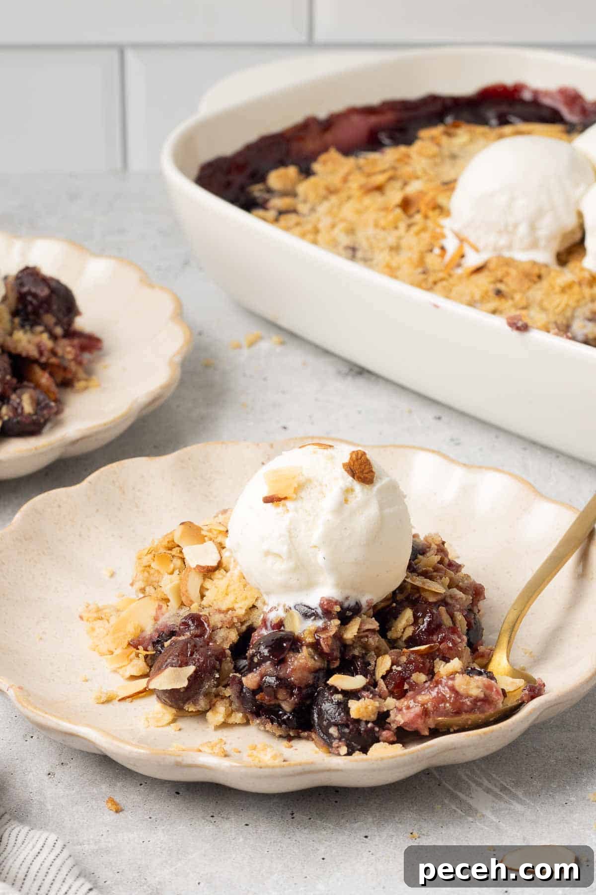 Cherry crisp topped with a scoop of ice cream on a plate with a spoon.