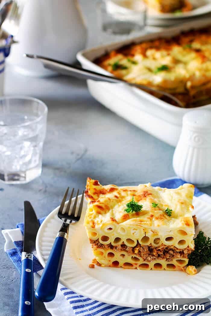 Classic Greek Pastitsio Recipe: Savory Baked Pasta Casserole 7 A serving of noodle moussaka on a white plate on blue-gray background and white dishes.