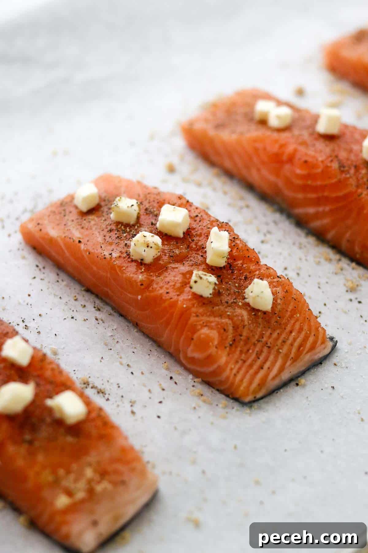 Brown Sugar Butter Baked Salmon with Garlic and Lemon 4 Unbaked salmon filets on parchment paper dotted with small pieces of butter.