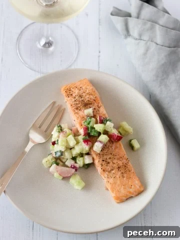 Salmon and cucumber radish relish on a plate with a fork, wine glass and napkin