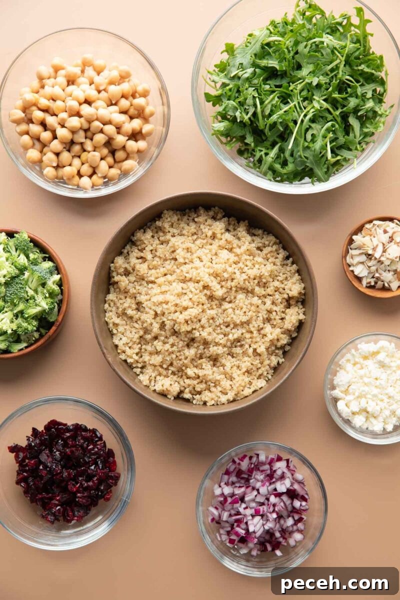 Lemony Quinoa and Arugula Salad with Cherry Tomatoes 3 mixing bowls with salad ingredients: cooked quinoa, chickpeas, arugula, chopped broccoli, sliced almonds, crumbled feta cheese, dried cranberries, and chopped red onions