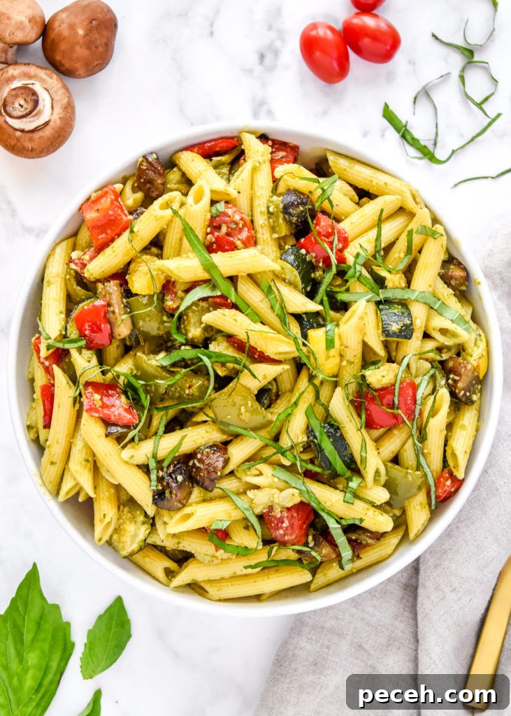 roasted veggie pesto pasta salad in a bowl with basil on top.