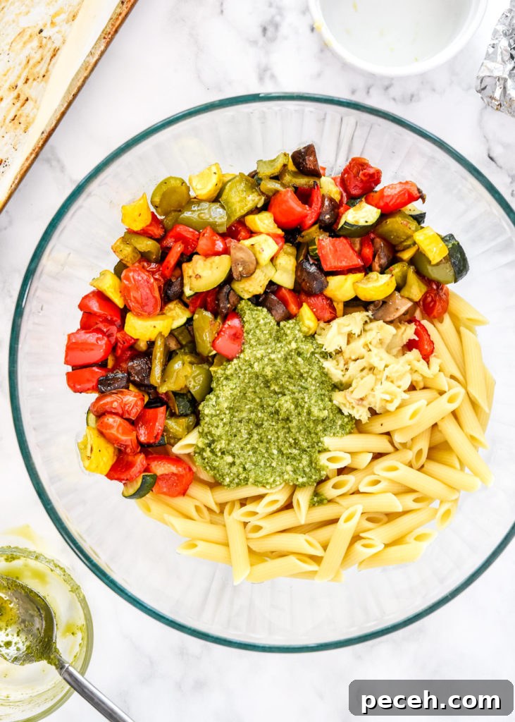 roasted vegetables, pasta and pesto in a large bowl before mixing.