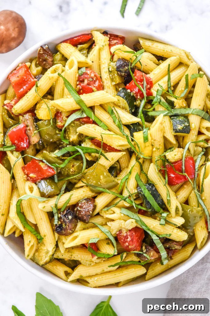 roasted veggie pesto pasta salad in a bowl with basil on top.