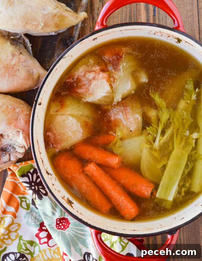 Carrots, celery and onions cooked in a Dutch oven with cooked chicken and a colorful napkin beside the pot.