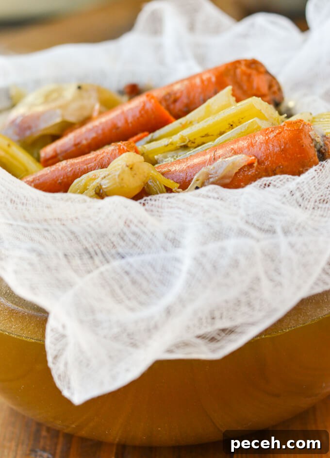 Cook carrots, celery and onions sitting a cheese cloth and metal mesh strainer with strained out chicken stock sitting in the bowl under need it.