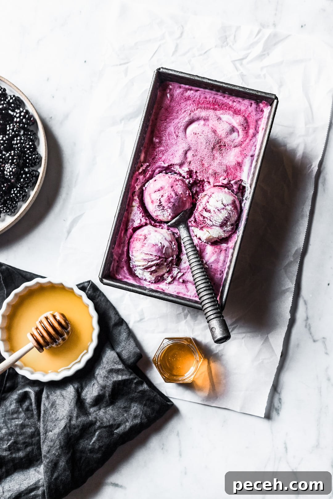 Honey-Blackberry Mascarpone Ice Cream Recipe 2 Three scoops of purple ice cream in container on a marble background with honey and blackberries nearby