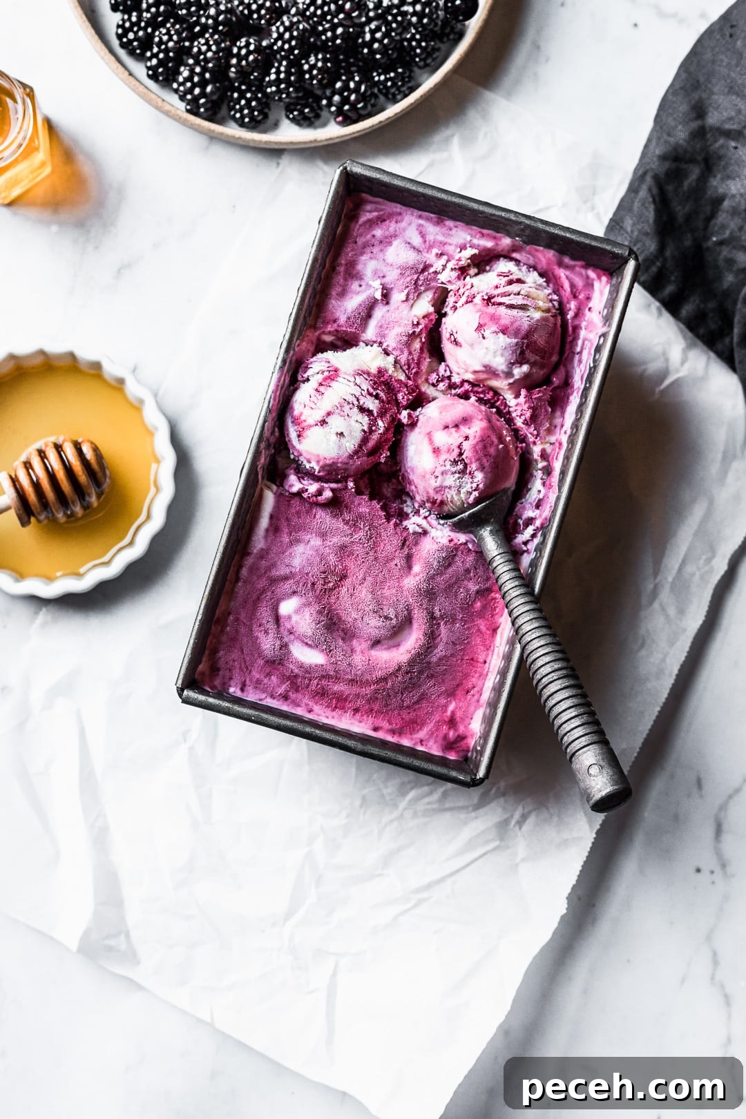 Honey-Blackberry Mascarpone Ice Cream Recipe 11 Three scoops of purple ice cream in container on a marble background with honey and blackberries nearby