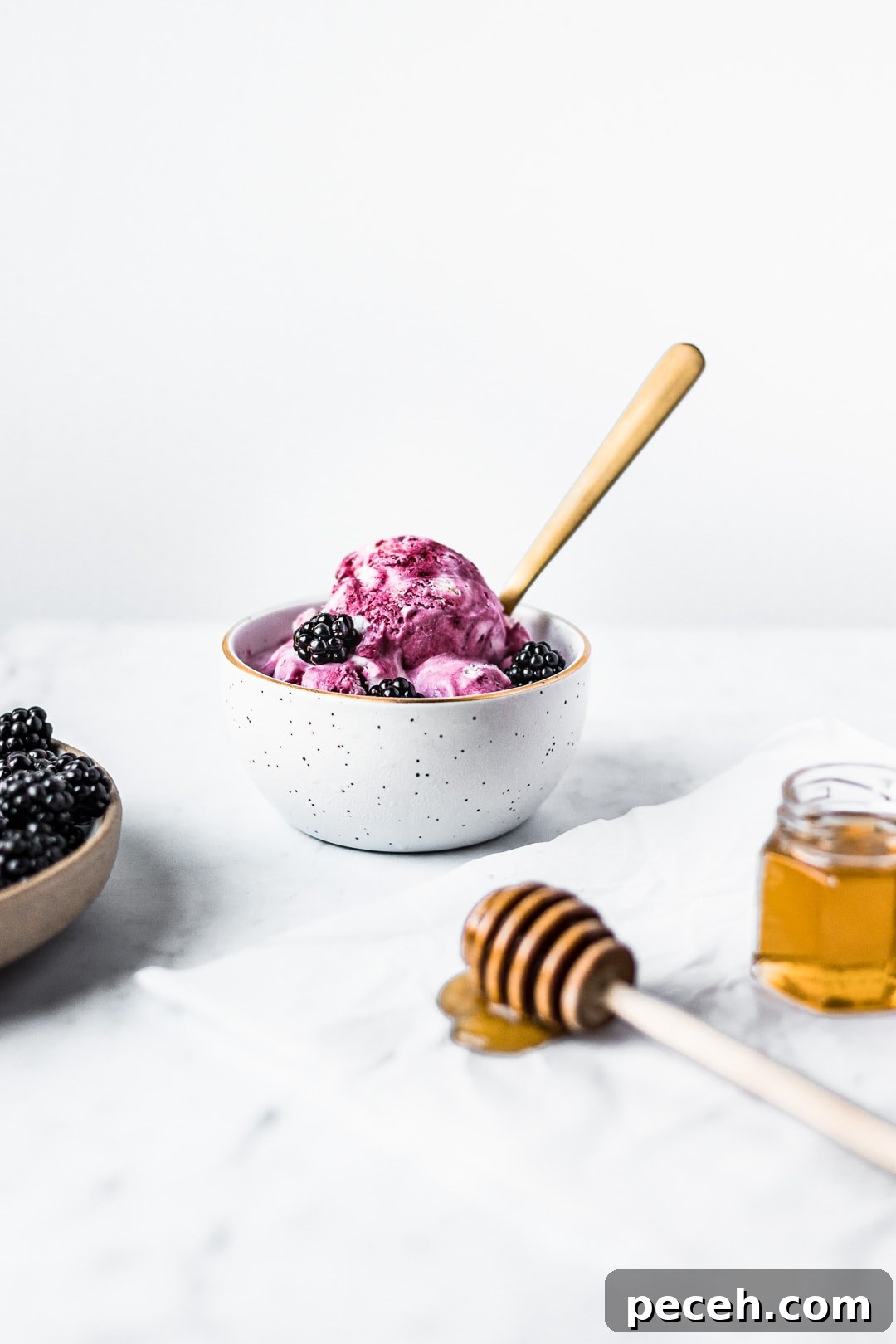 Honey-Blackberry Mascarpone Ice Cream Recipe 12 Front view of honey blackberry mascarpone ice cream scoops in a bowl with blackberries and honey in foreground