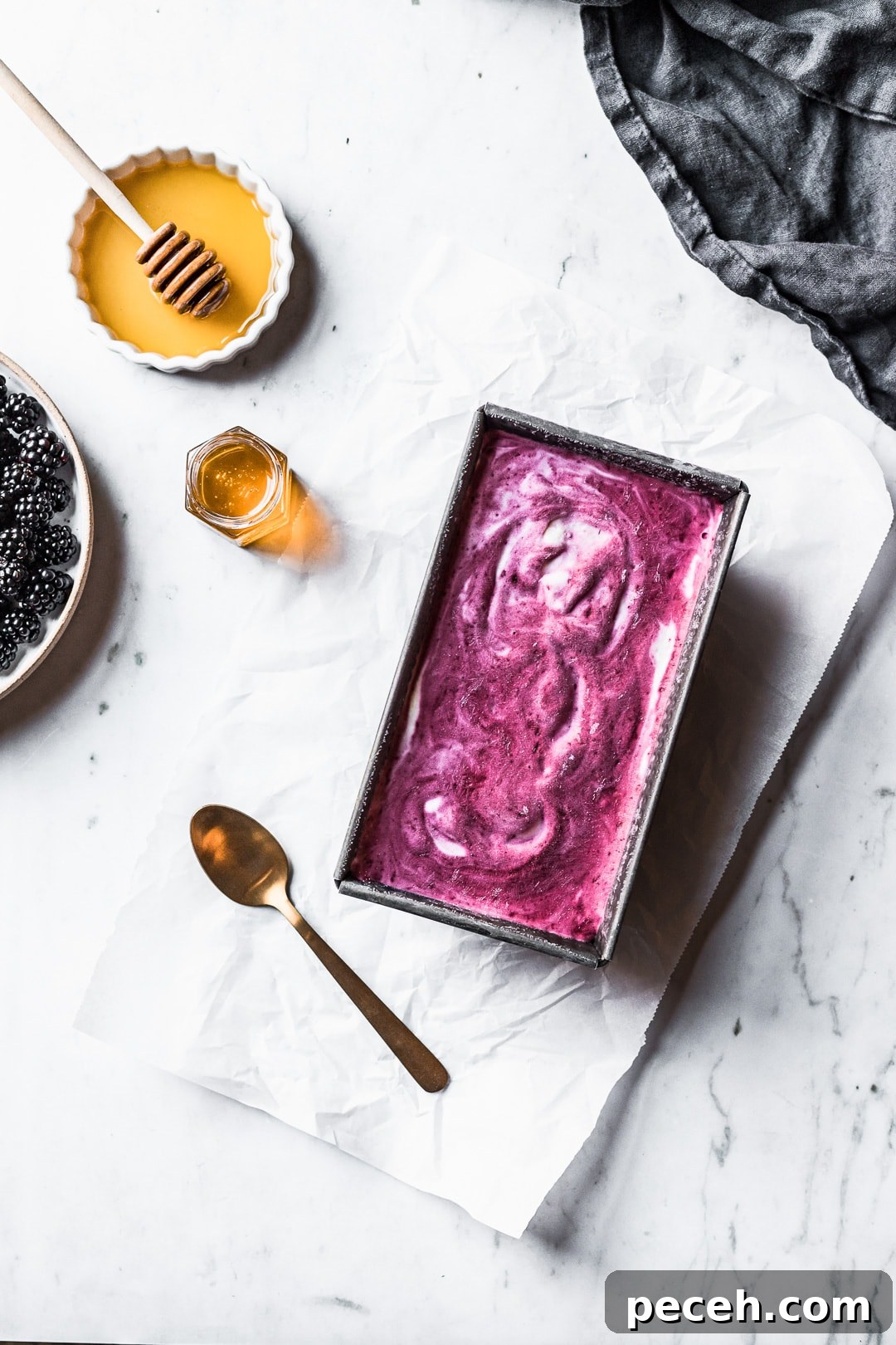 Honey-Blackberry Mascarpone Ice Cream Recipe 4 Purple and white swirled ice cream in a container on a marble background with blackberries and honey nearby