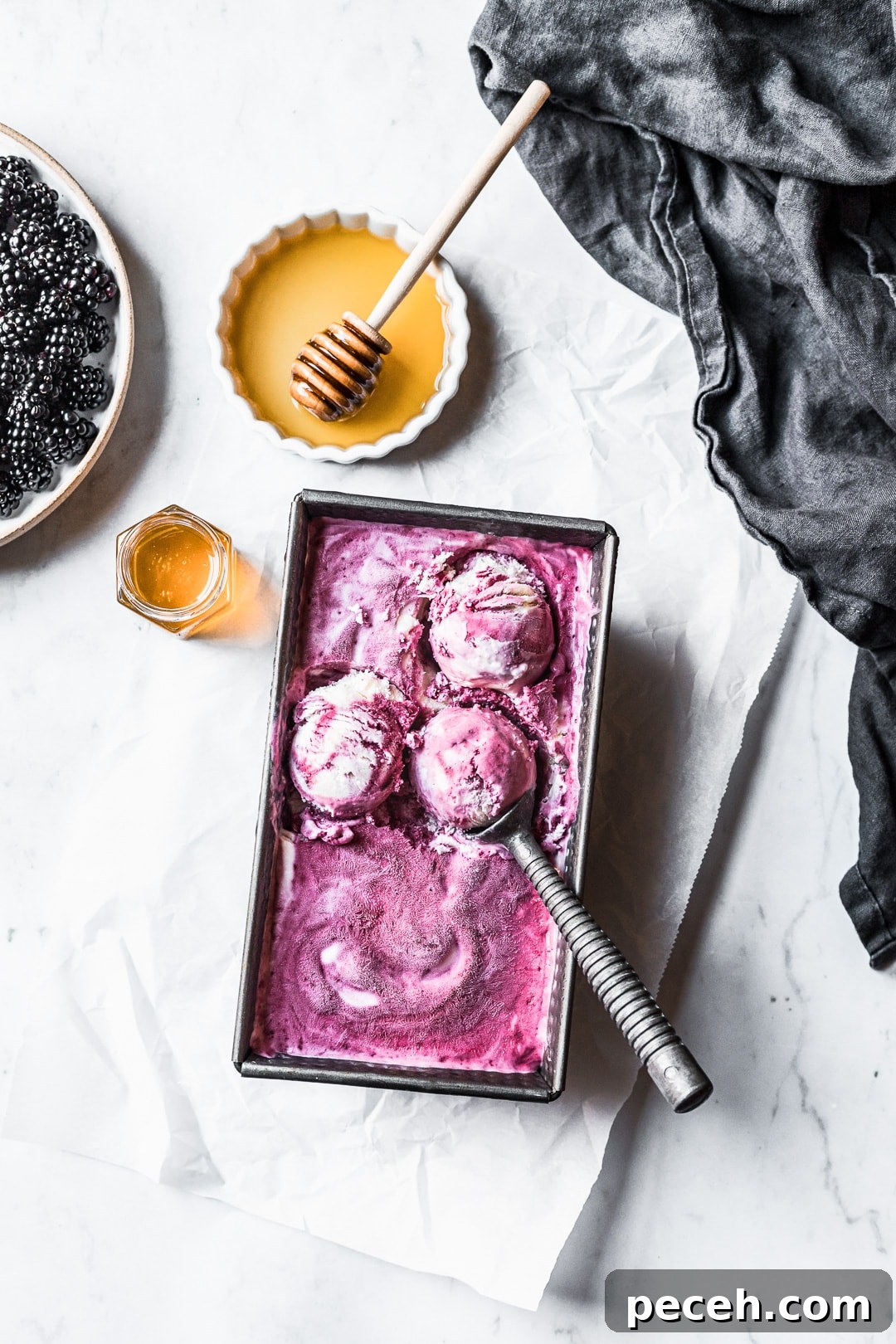 Honey-Blackberry Mascarpone Ice Cream Recipe 5 Three scoops of purple ice cream in container on a marble background with honey and blackberries nearby