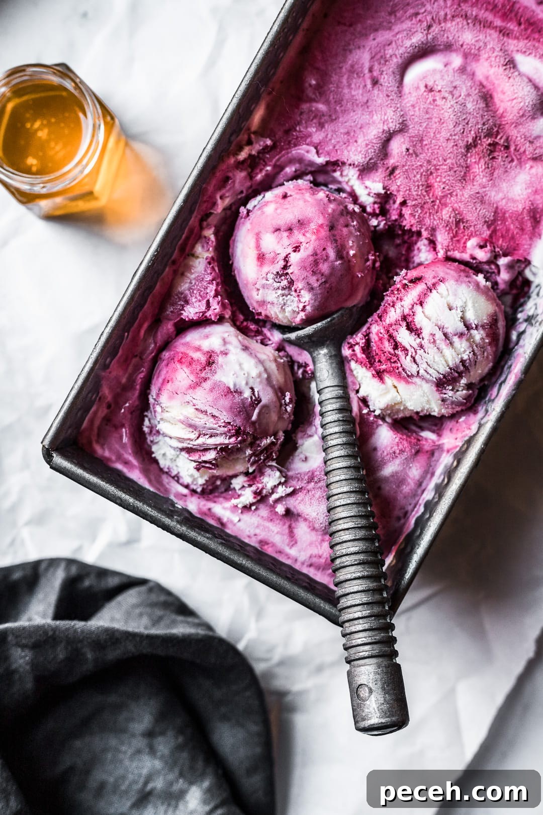 Honey-Blackberry Mascarpone Ice Cream Recipe 6 Three scoops of purple and white ice cream in a container on parchment paper with honey nearby