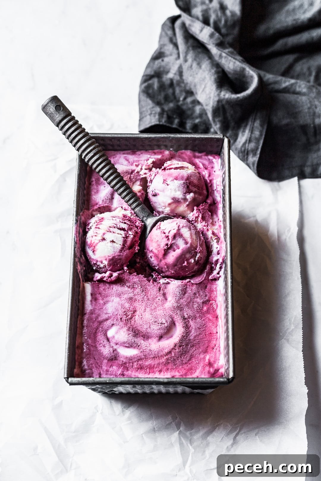 Honey-Blackberry Mascarpone Ice Cream Recipe 8 Angled view of purple and white swirled ice cream with three scoops shaped and ice cream scoop resting on container