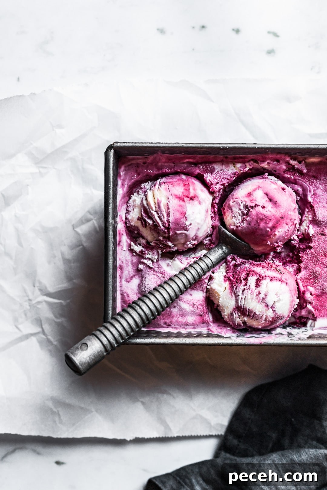 Honey-Blackberry Mascarpone Ice Cream Recipe 10 Closeup of three scoops of purple and white blackberry mascarpone ice cream in a container with the scoop resting on top