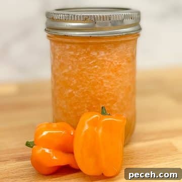Pineapple habanero sauce in a glass jar with two habaneros on a butcher block counter.