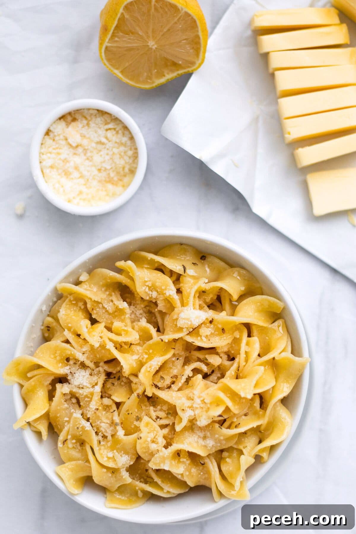 butter noodles in a bowl with butter, parm and lemon around it.