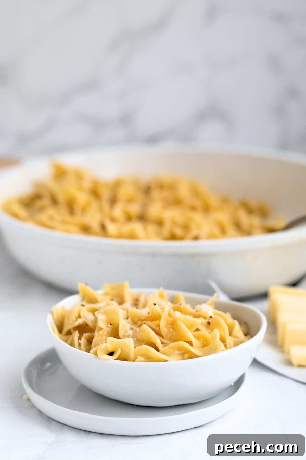 butter noodles in a white bowl with pan behind it.