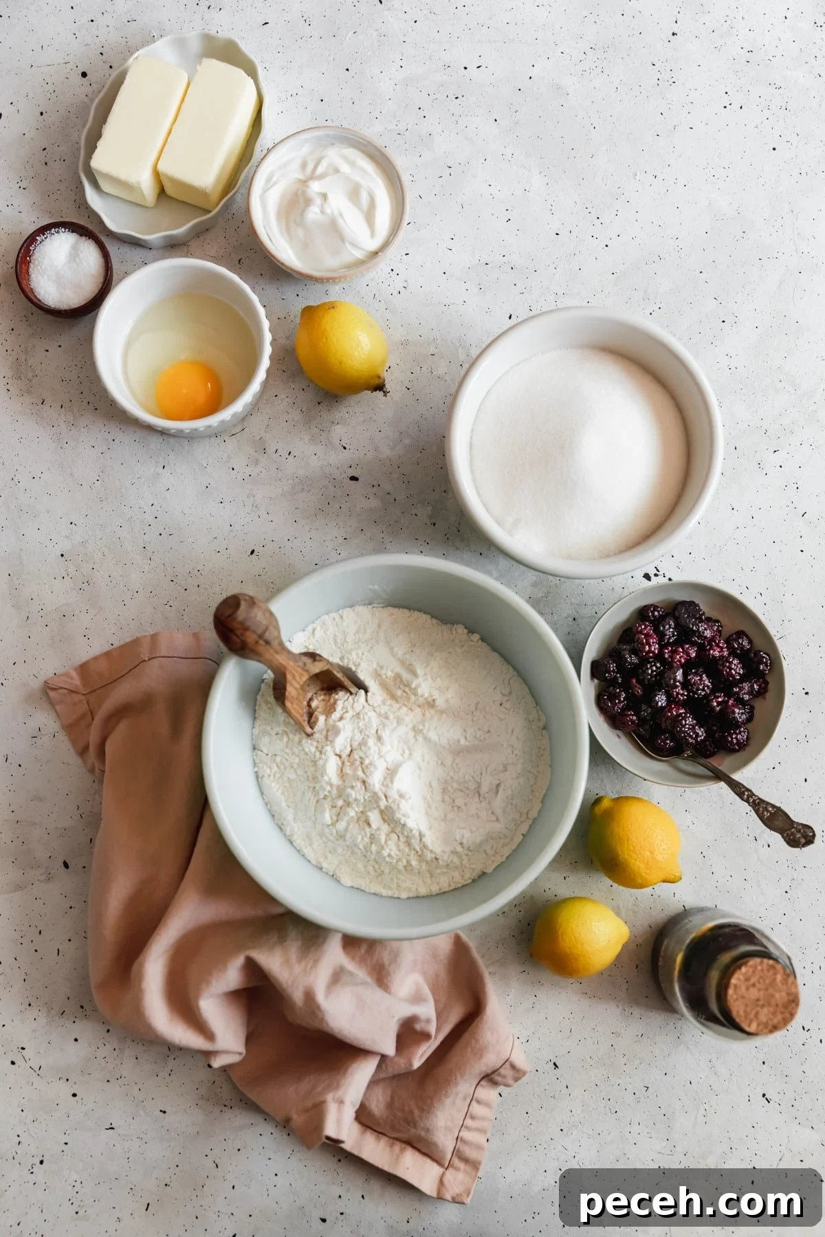 Lemon Sour Cream Pound Cake with Blackberry Glaze 4 An overhead image of ingredients for sour cream lemon pound cake in various white and grey bowls on a white speckled table next to a bowl of blackberries, lemons, and a pink linen.