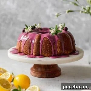 Lemon Sour Cream Pound Cake with Blackberry Glaze 9 A side image of a pound cake with pink glaze on a marble cake stand with a grey background and lemons to the side.