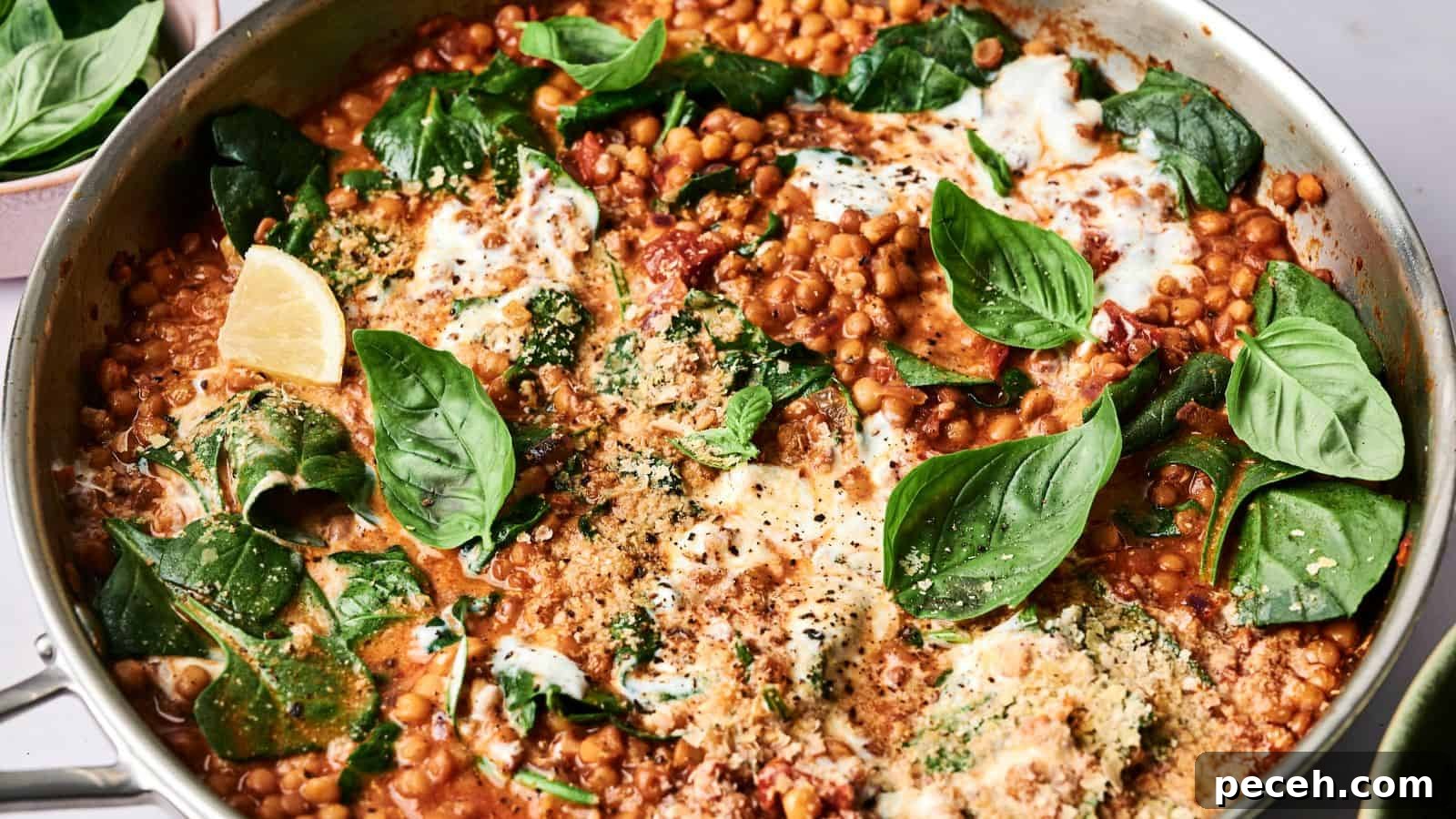 A pan of lentil dish with spinach, fresh basil, tomato sauce, and melted cheese, garnished with lemon wedges.