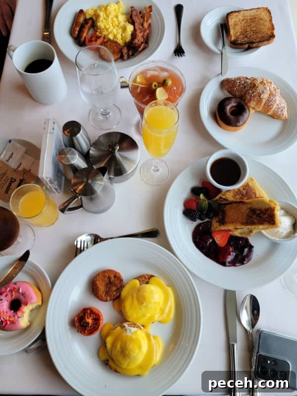 3-Night Royal Caribbean Navigator of the Seas Cruise to Ensenada 9 breakfast spread over a white table cloth including eggs benedict, French toast, a donut, croissant, Bloody Mary and Orange Juice