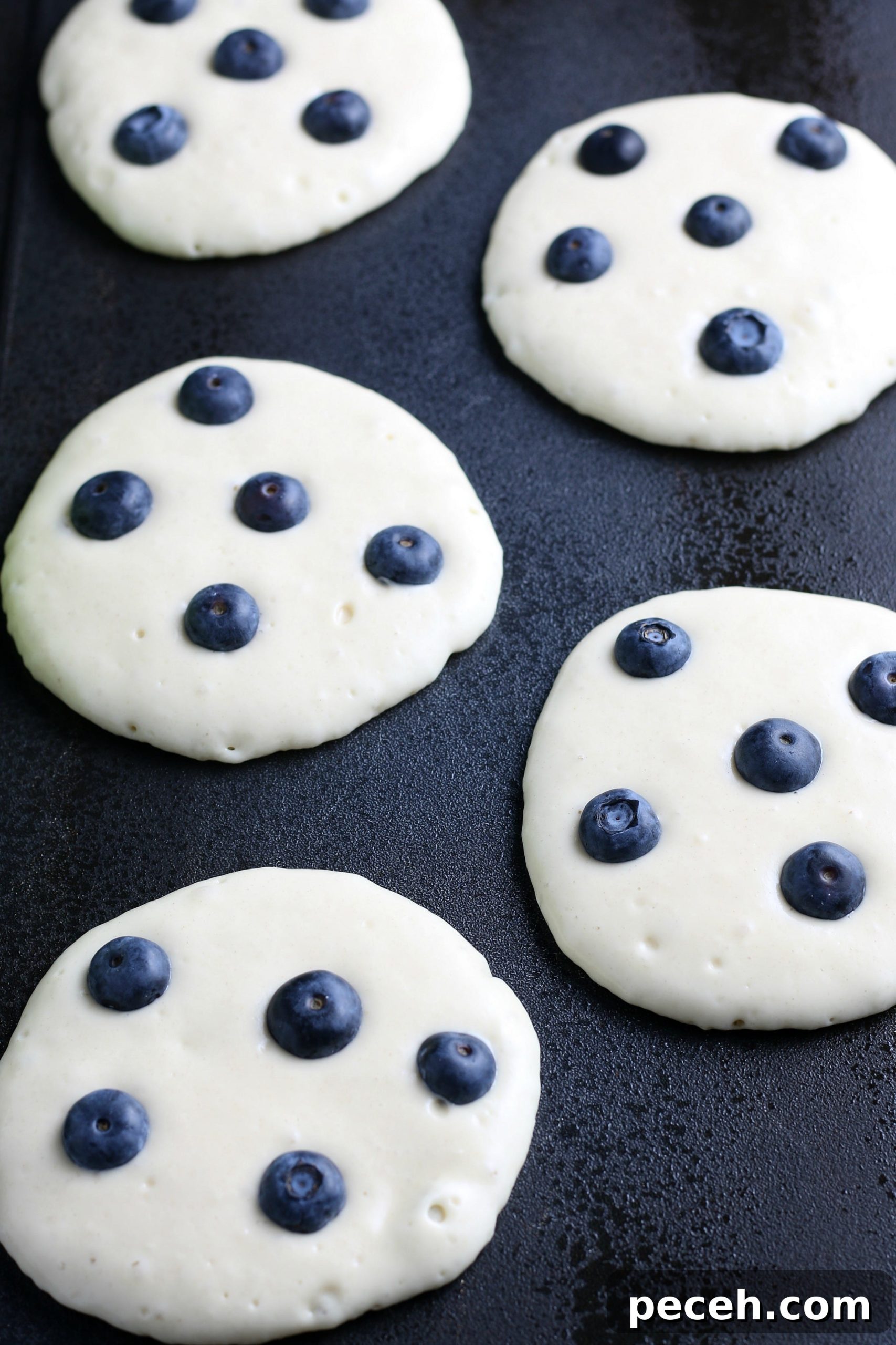 Homemade Blueberry Pancake Recipe for Fluffy, Perfect Stacks 6 blueberry pancakes on a griddle