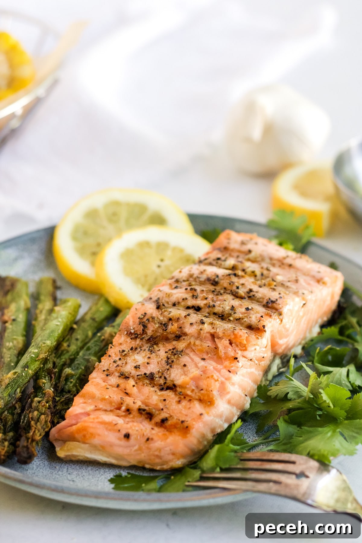 Perfectly Grilled Salmon with Crispy Skin and Lemon Herb Rub 2 Grilled salmon on a grey plate with herbs and sliced lemons.