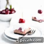 slice of black forest cheesecake on a white and blue plate placed at an angle so you can see layers of whipped cream, chocolate cheesecake and cherry compote.