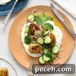 Chicken koftas on top of yogurt with herbs and cucumbers on a beige plate.