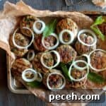 Chicken kebabs on a parchment lined pan topped with onion rings.