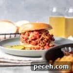Ground chicken sloppy Joe filled to the brim on a hamburger bun next to pickle slices.